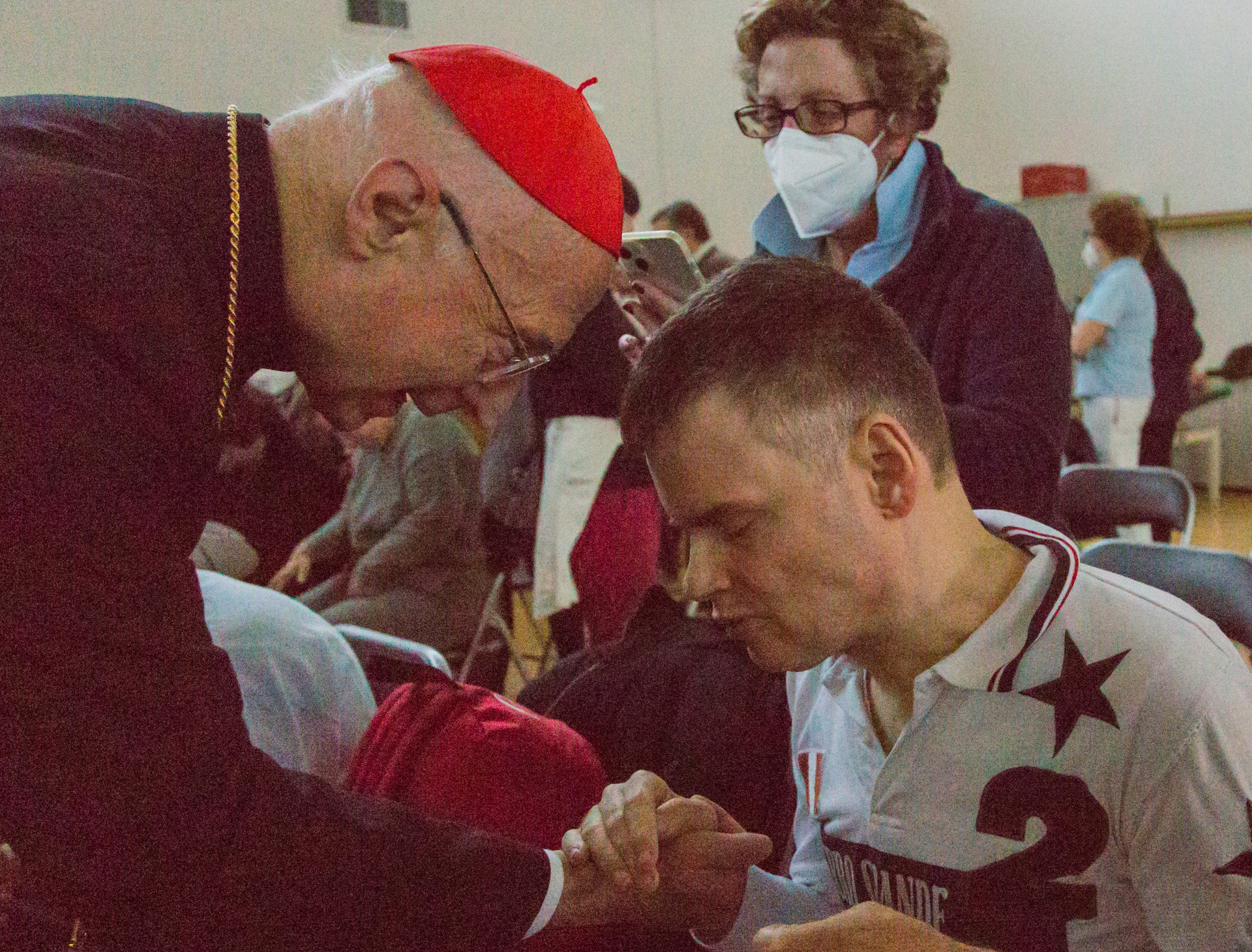 Il Cardinale Angelo Bagnasco è ritratto mentre saluta con affetto un utente della Lega del Filo d’Oro, stringendogli la mano.