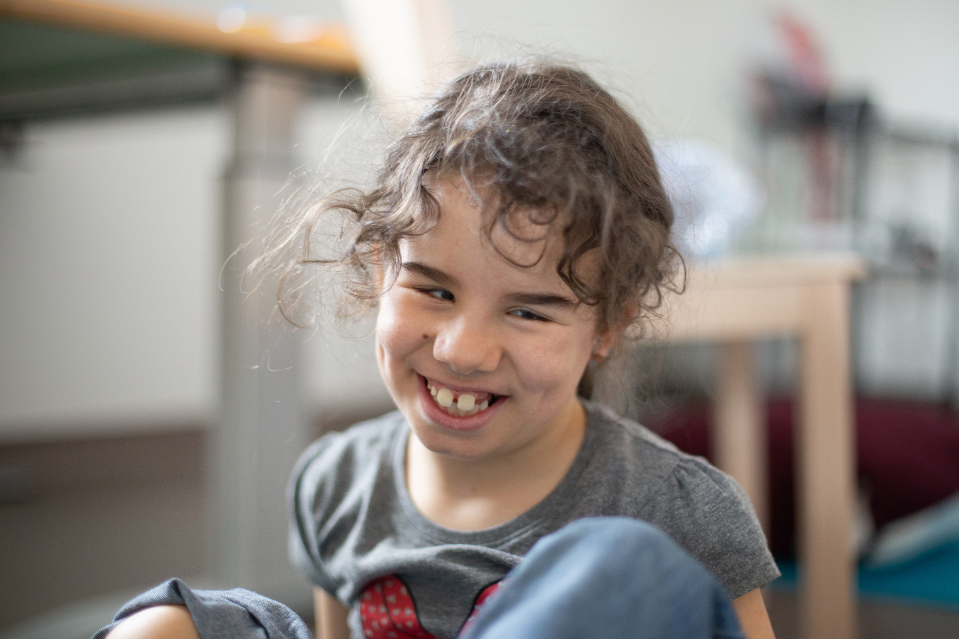 Giulia, bambina sordocieca di 8 anni seguita al Centro di Osimo, è seduta sul pavimendo di un'aula educativa del Centro Nazionale e sorride