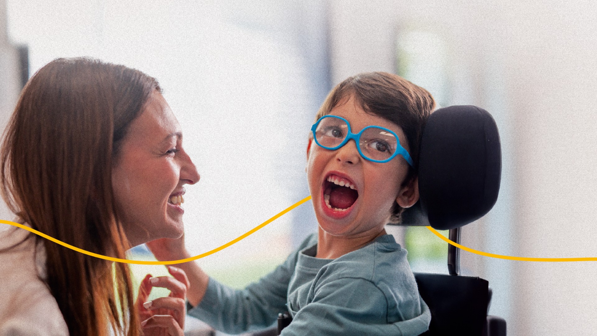 Nicola, bambino utente della Lega del Filo d’Oro, sorride in primo piano, assieme a Claudia una sostenitrice.