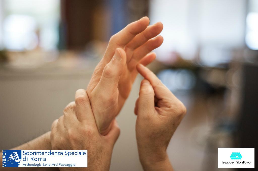 Sono fotografate le mani di due persone che comunicano con il metodo Malossi. Alla base dell'immagine sono inseriti due loghi: Soprintendenza Speciale di Roma e Lega del Filo D'Oro