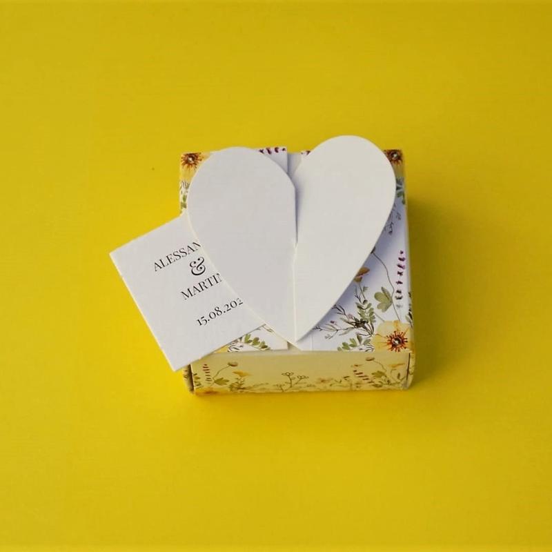 Bomboniera Floreale Lega del Filo d'Oro, in cartoncino bianco con una fantasia a fiori di campo e una romantica chiusura a cuore.