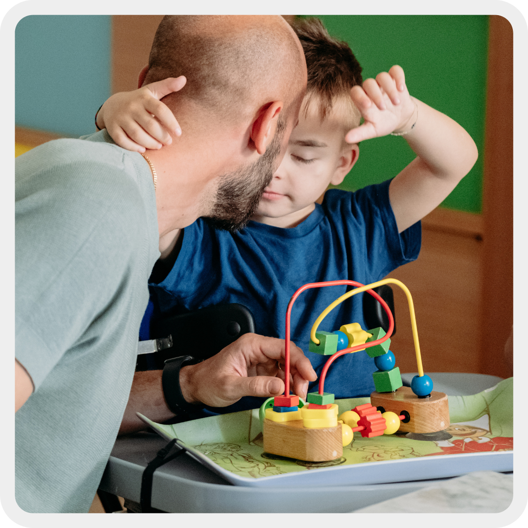 Edoardo, bambino con disabilità uditive e motorie, insieme al suo papà. Edoardi allunga le braccia alla ricerca di un abbraccio in una scena tenera e commovente.