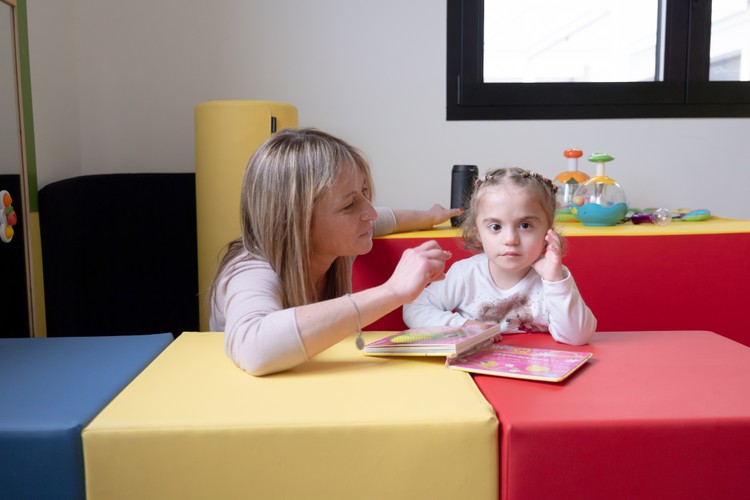 Benedetta e Romina, una bambina utente della Lega del Filo d'Oro, sfogliano un libro usando come tavolo di appoggio dei cubi colorati.
