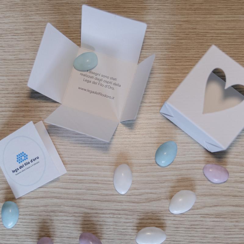 Bomboniera Cubo Pop aperta per mostrare le parti di cui si compone e la scritta interna che spiega la scelta di ispirarsi per le fantasie ai disagni degli ospiti della Lega del Filo d'Oro