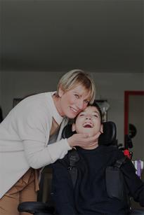 Bambino della Lega del Filo d'Oro sorridente abbracciato amorevolmente, mentre sorride.