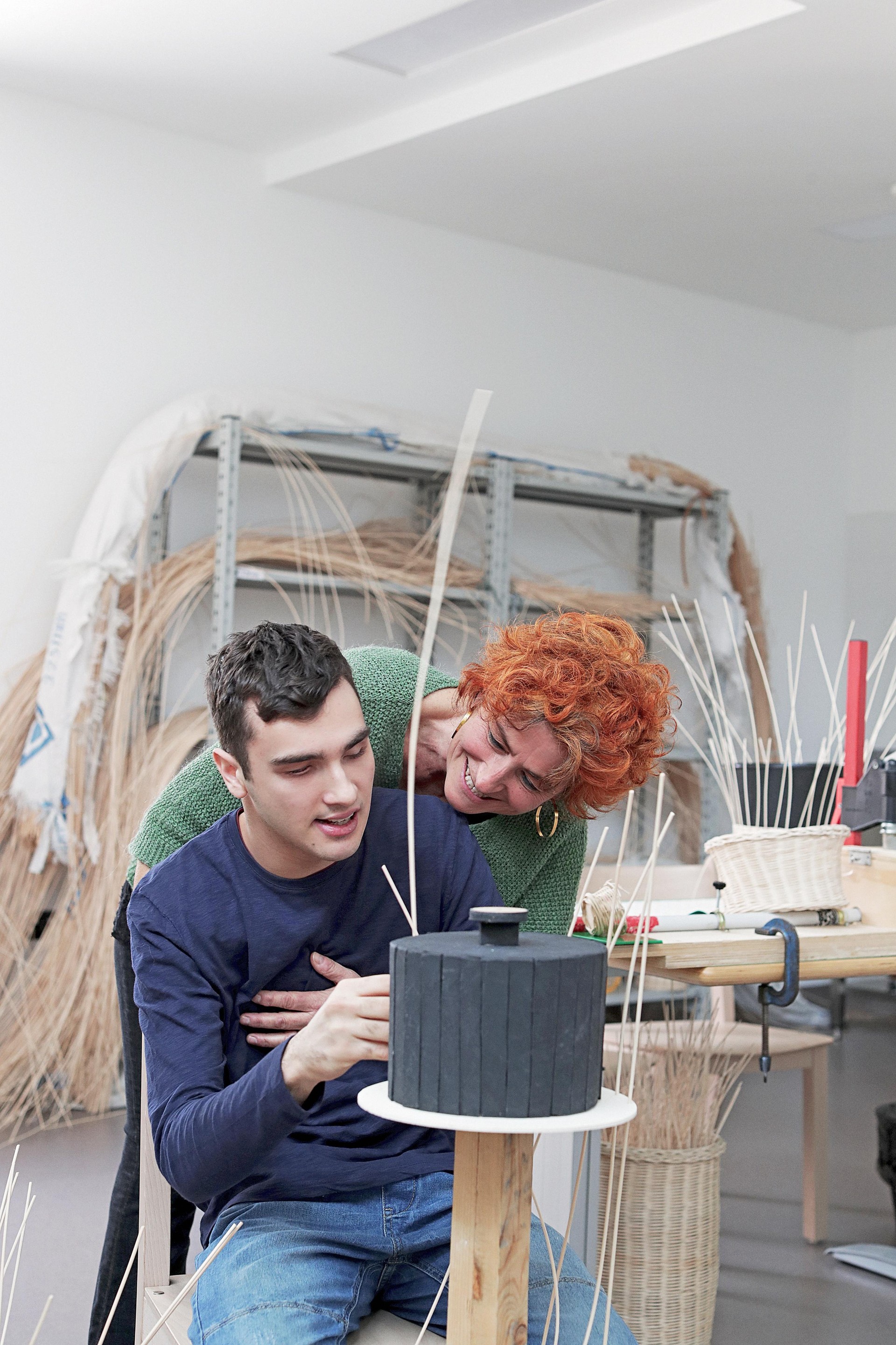 Francesco, giovane utente del Centro Diurno di Osimo, è al lavoro nel laboratorio di midollino. La sua educatrice, alle sue spalle, lo abbraccia sorridendo