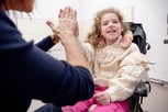 Melissa è seduta sulla sua sedia a rotelle e batte il cinque alla sua educatrice che è difronte a lei