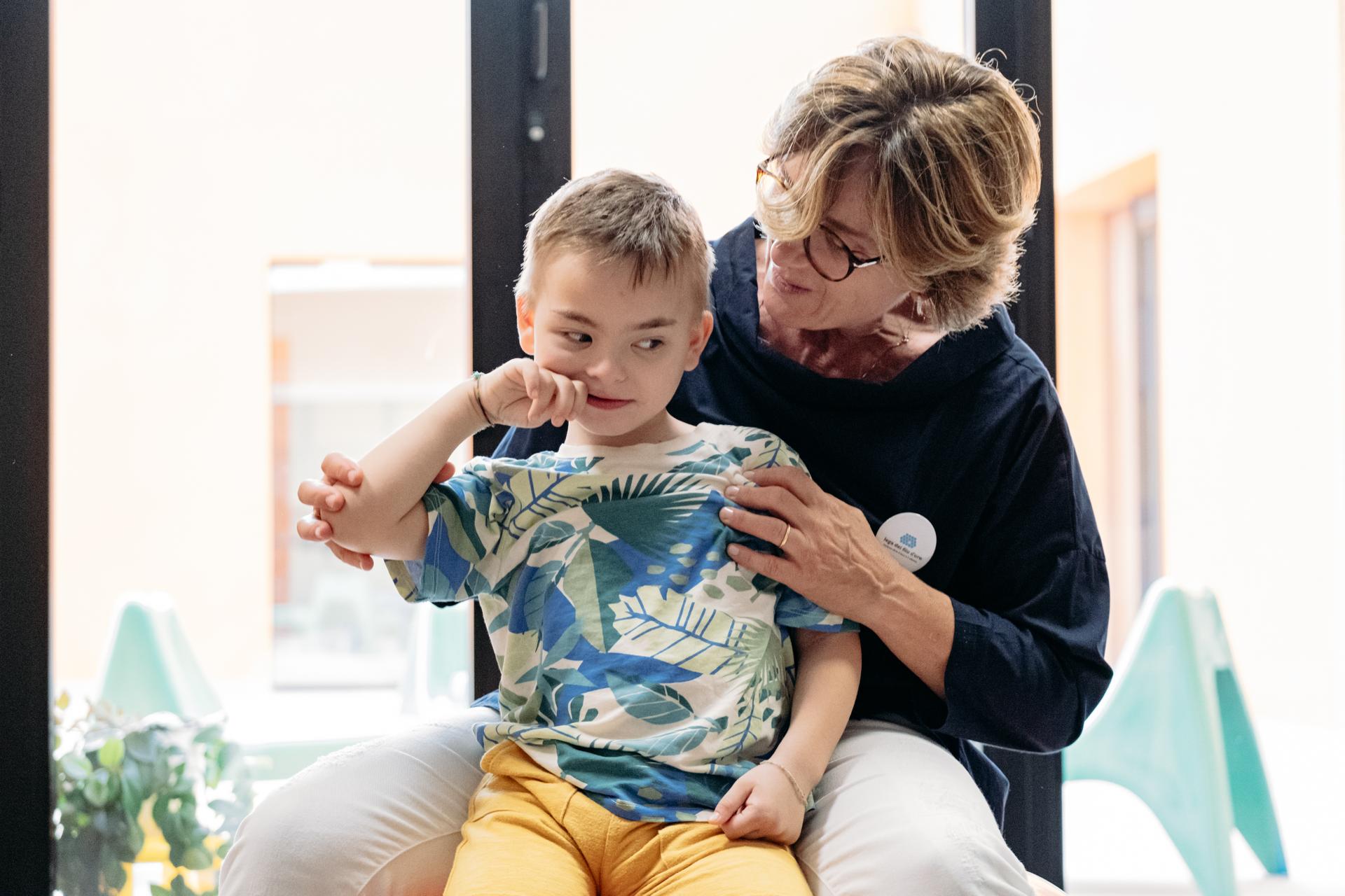 Edoardo insieme alla sua educatrice. Edoarso è sedutosulle gambe dell'educatrice che lo abbraccia. Lo sguardo è assorto 