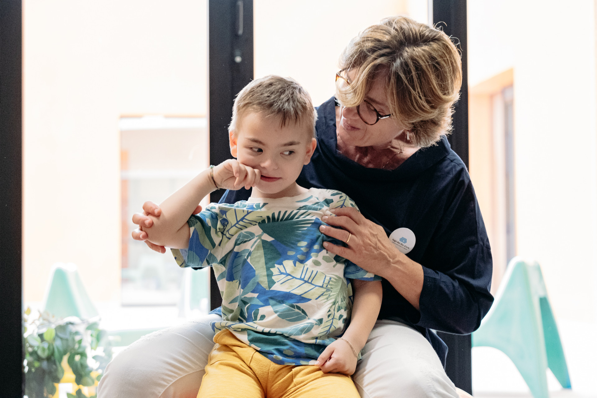Edoardo insieme alla sua educatrice. Edoarso è sedutosulle gambe dell'educatrice che lo abbraccia. Lo sguardo è assorto 