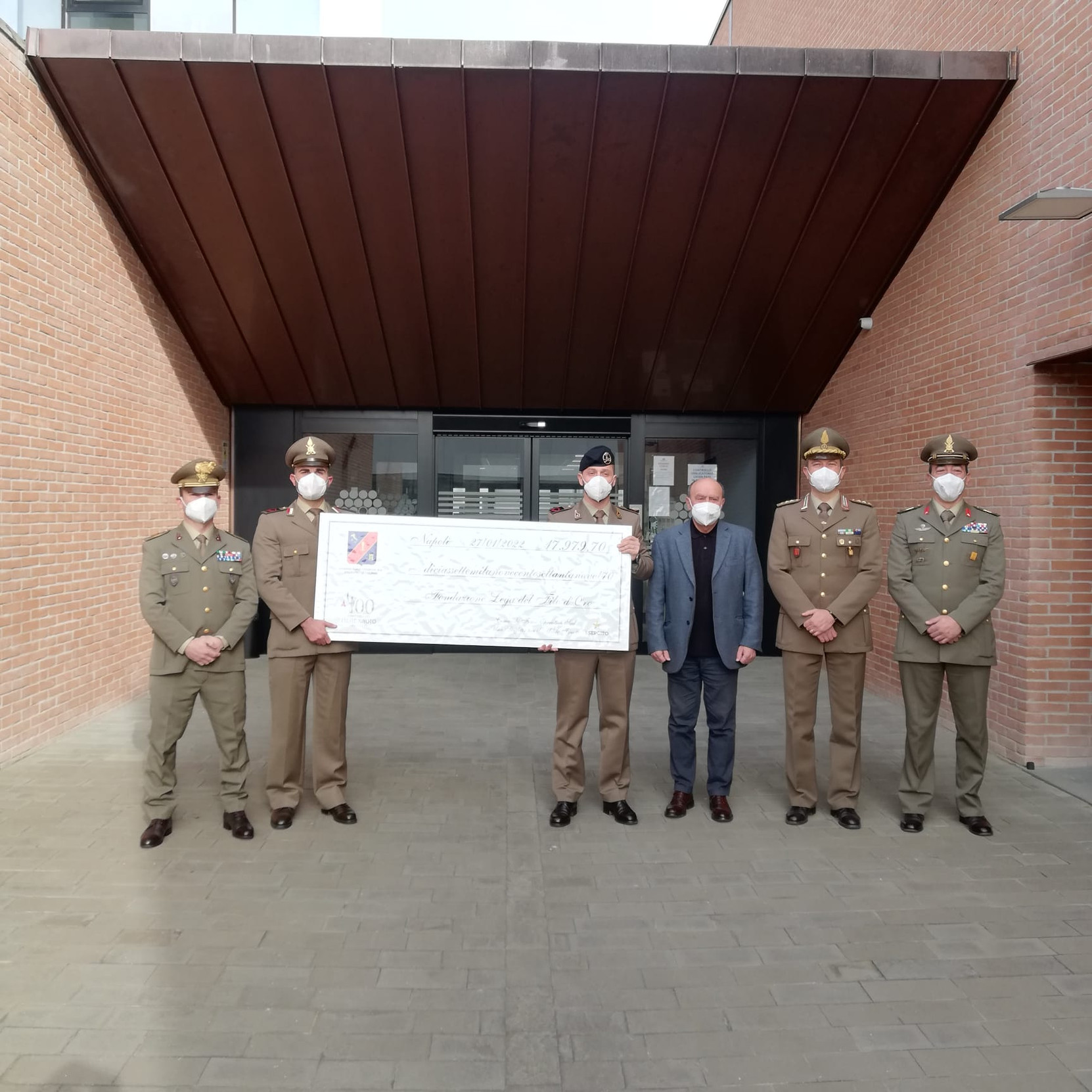 Nella foto ci sono 5 militari, insieme a Rossano Bartoli Presidente della lega del filo d'oro, che reggono un assegno di beneficenza.