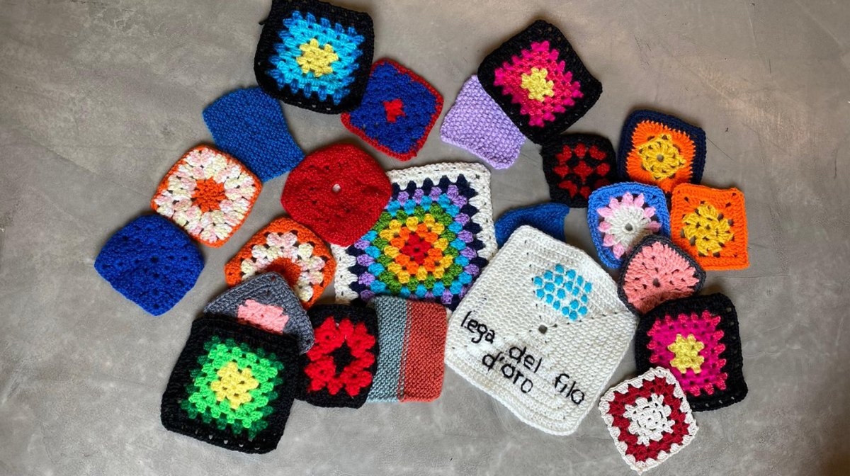 Tante pezze di maglia colorate e a forma di quadrato sono sparse su una superficie grigia. 