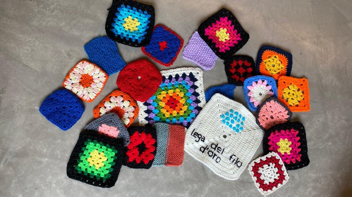 Tante pezze di maglia colorate e a forma di quadrato sono sparse su una superficie grigia. 