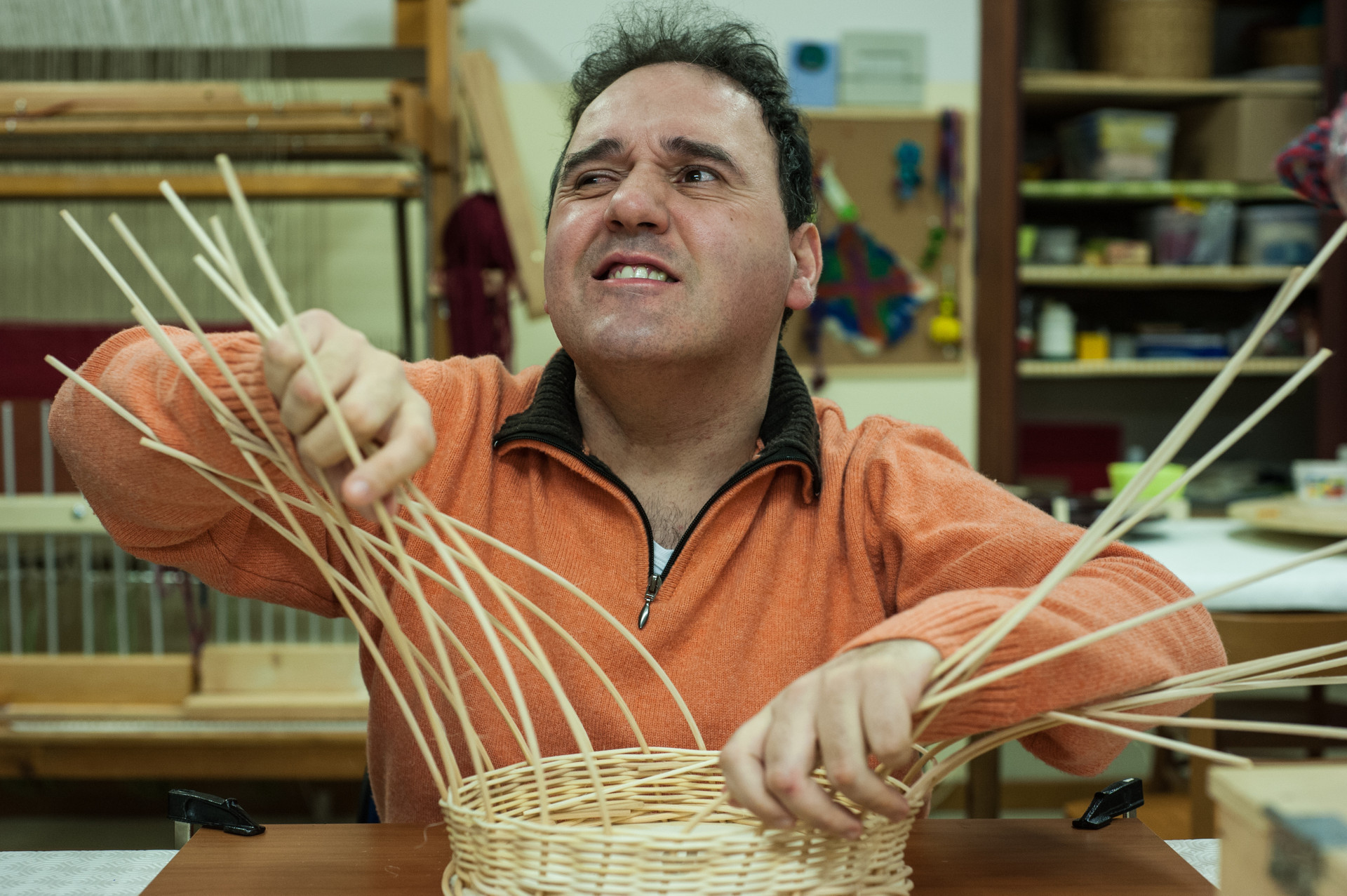 Alberto utente adulto è impegnato nella realizzazione di un cestino di midollino all'interno del laboratorio di cestineria della Lega del Filo d'Oro