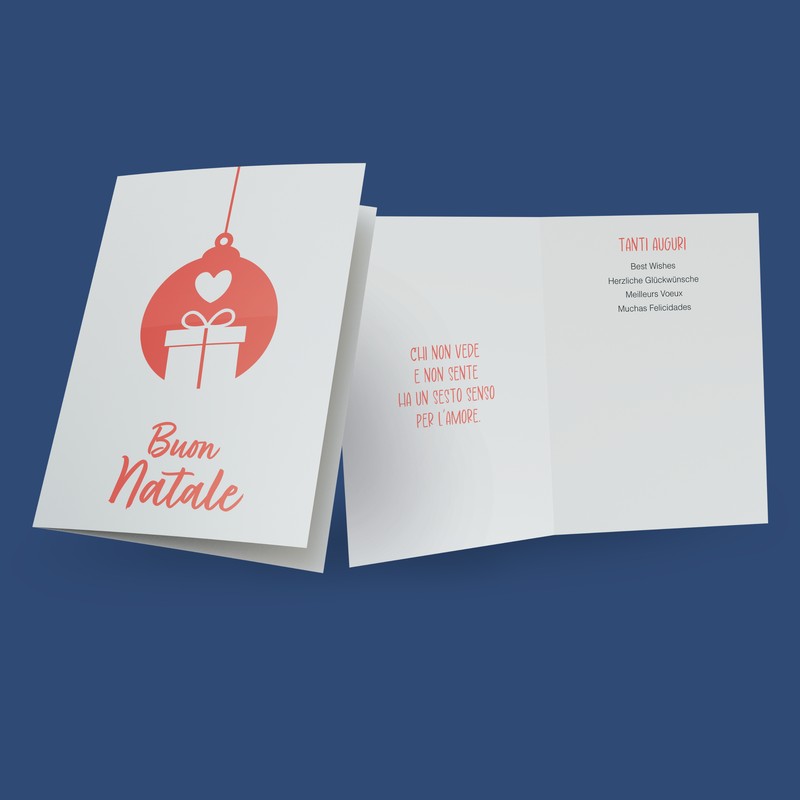 Il biglietto per augurare buone feste con raffigurata una grande pallina di Natale rossa con disegnato un pacchetto regalo bianco e un cuore. Sotto il disegno la scritta "Buon Natale". All'interno del biglietto è stampata la frase "Chi non vede e non sente ha un sesto senso per l'amore".