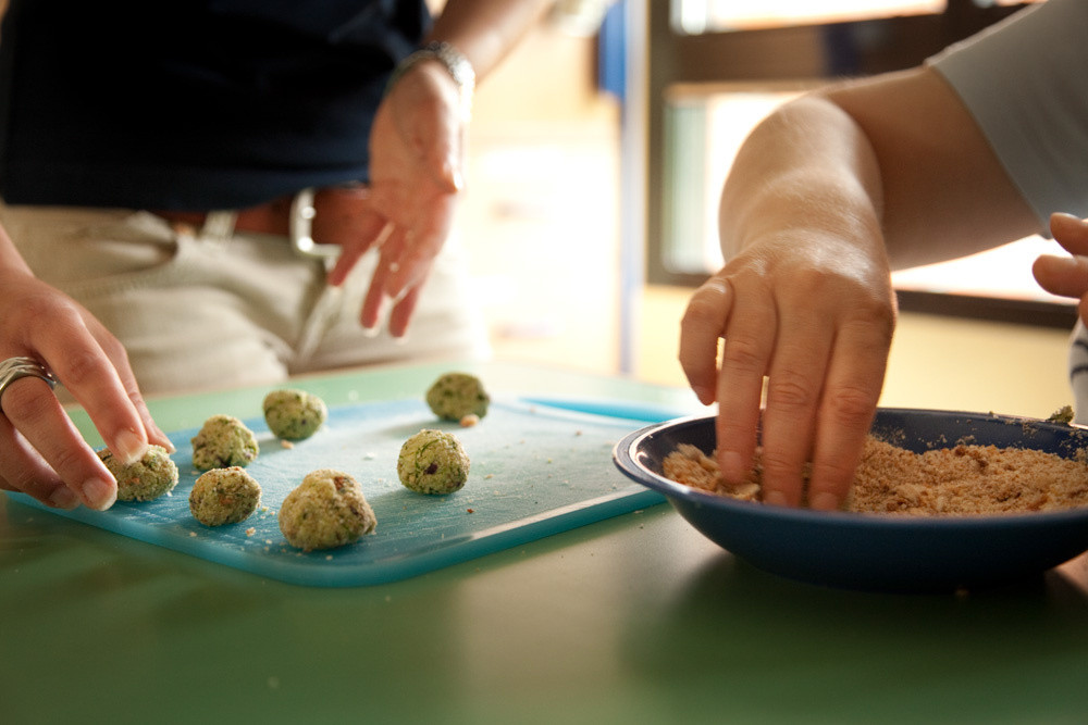 Dettaglio delle mani degli utenti nel corso di un'attività di cucina didattica. Preparano insieme delle polpette, ognuno occupandosi di una diversa operazione.