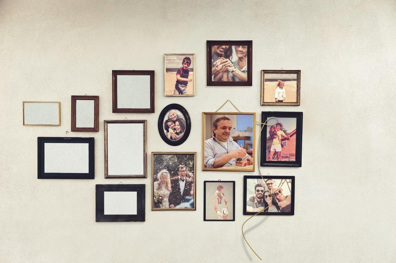 Un muro color giallino è decorato con diverse cornici: alcune vuote, altre con fotografie. Spicca una cornice contenente la foto di Fabio, elemento centrale della composizione.