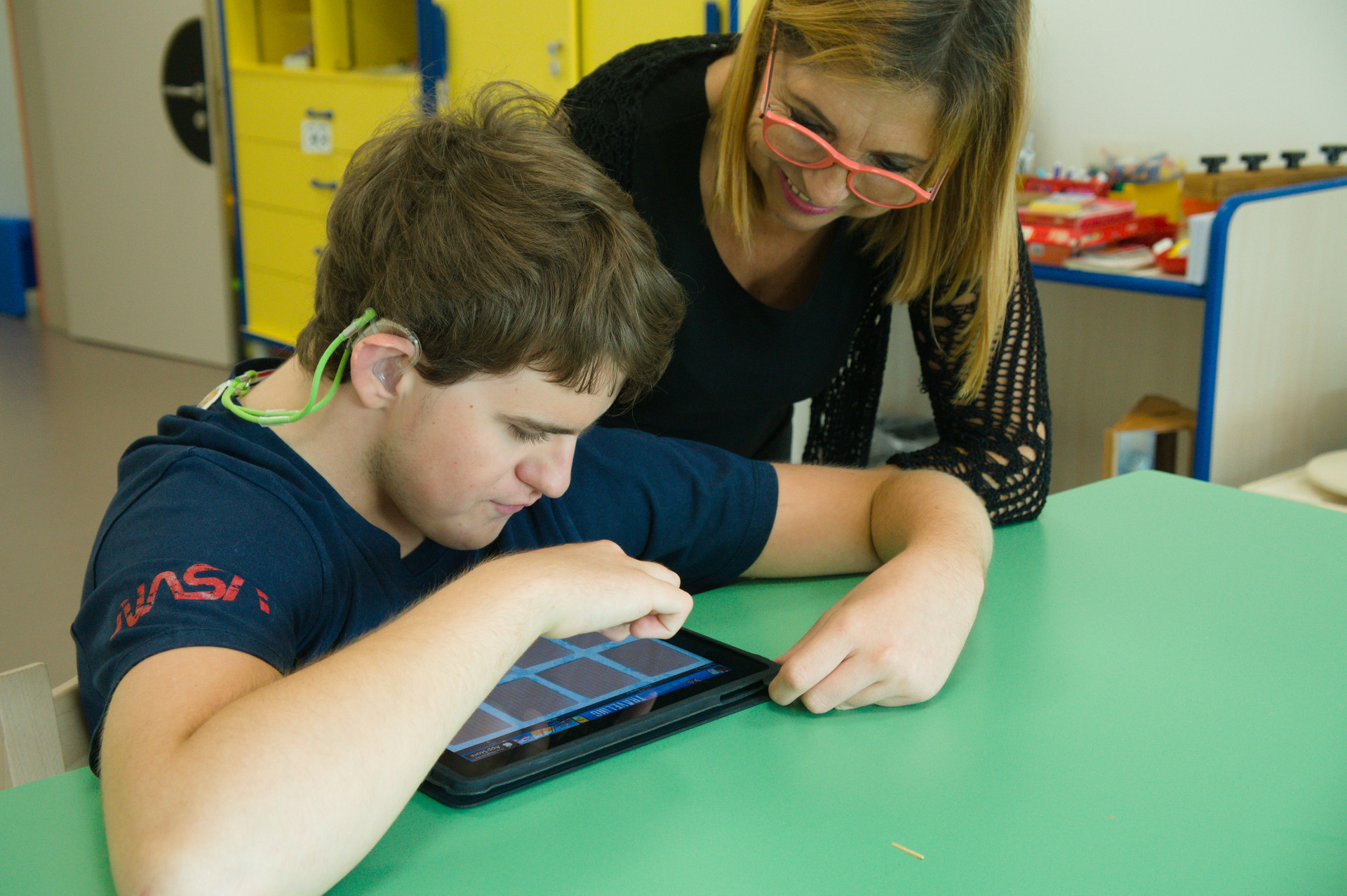 L'educatrice sorride guardando Thomas che svolge un'attività usando un tablet.