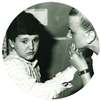 Alberto, un utente adulto della Lega del Filo d'Oro, in una foto da bambino che fa attività con la sua educatrice.