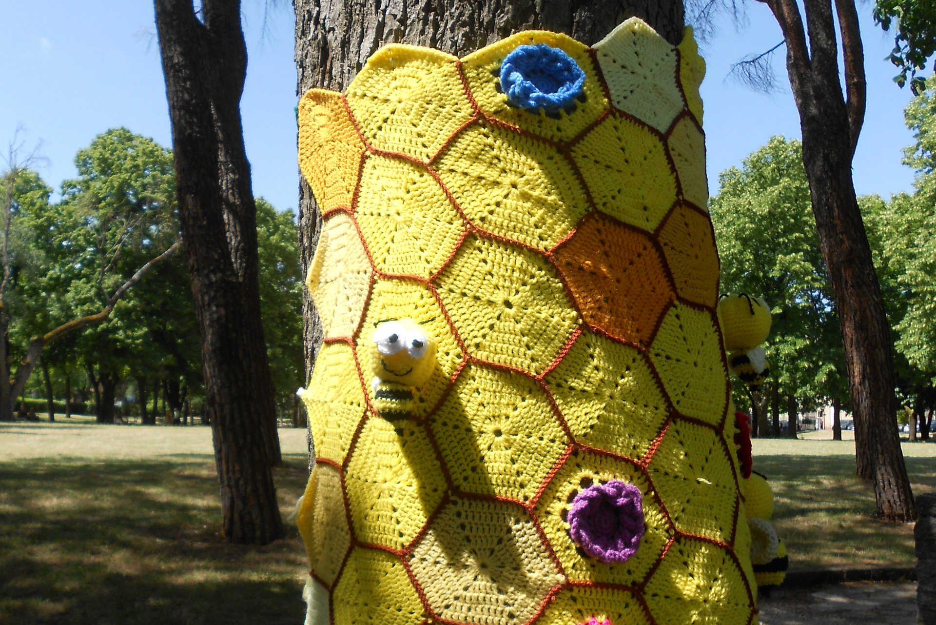 Foto di un lavoro di Yarn Bombing all'uncinetto che abbraccia un albero, creando un effetto colorato e artistico.
