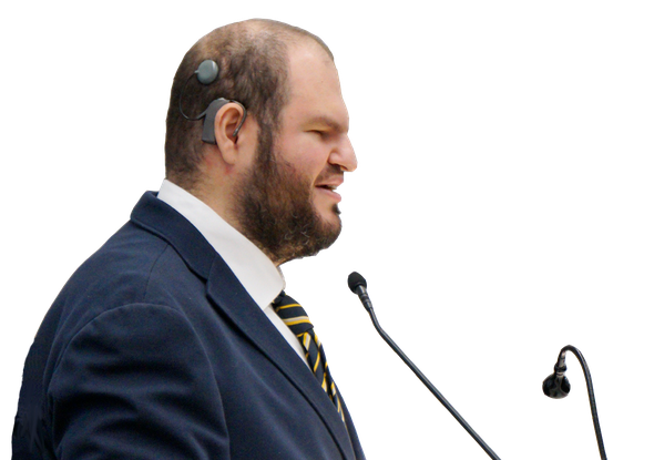 Francesco Mercurio, Presidente del Comitato delle Persone Sordocieche, è in piedi davanti a un piedistallo con due microfoni. È vestito in modo formale.