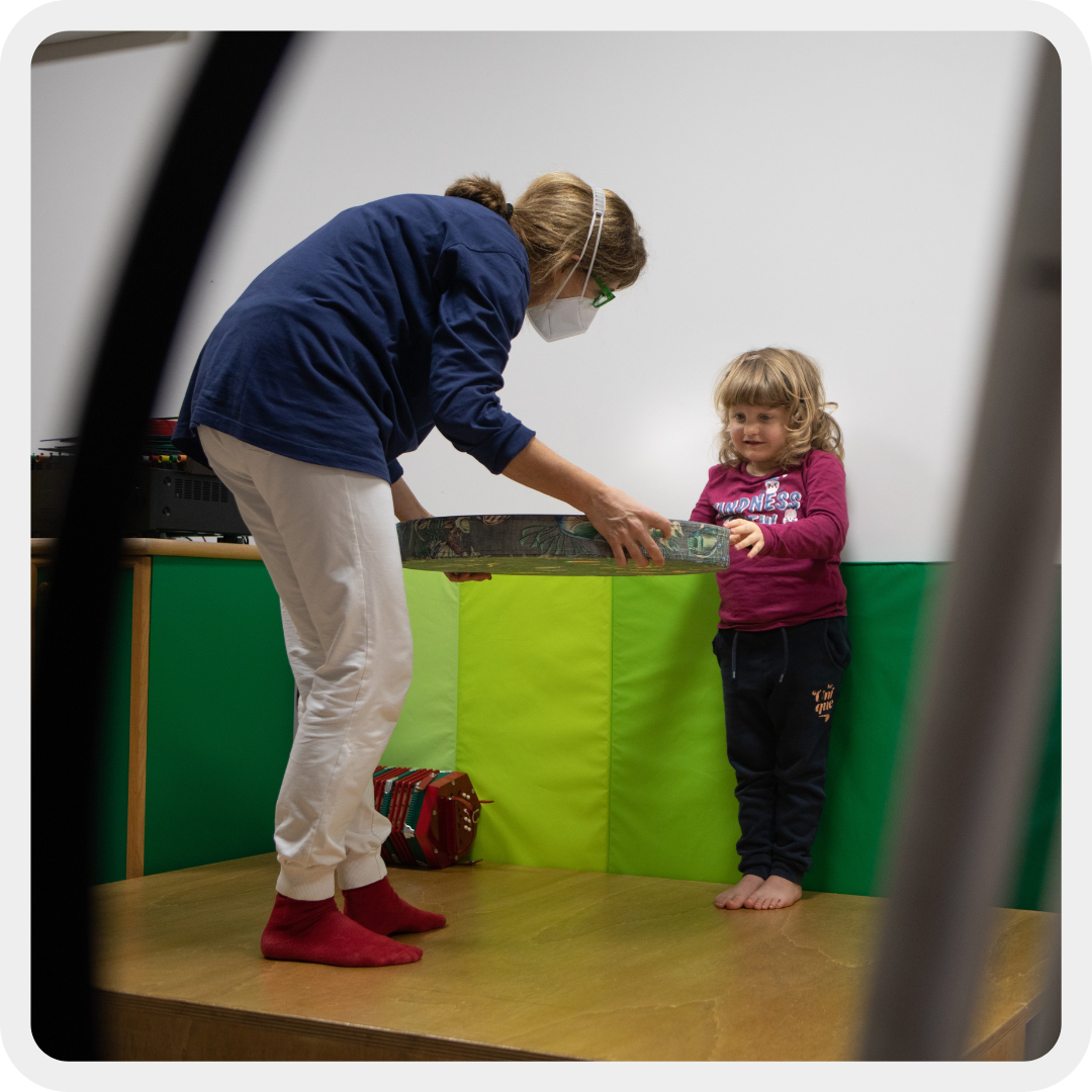 Bambina con disabilità visive e uditive durante una sessione di musicoterapia. La bambina è concentrata e coinvolta nell'attività.