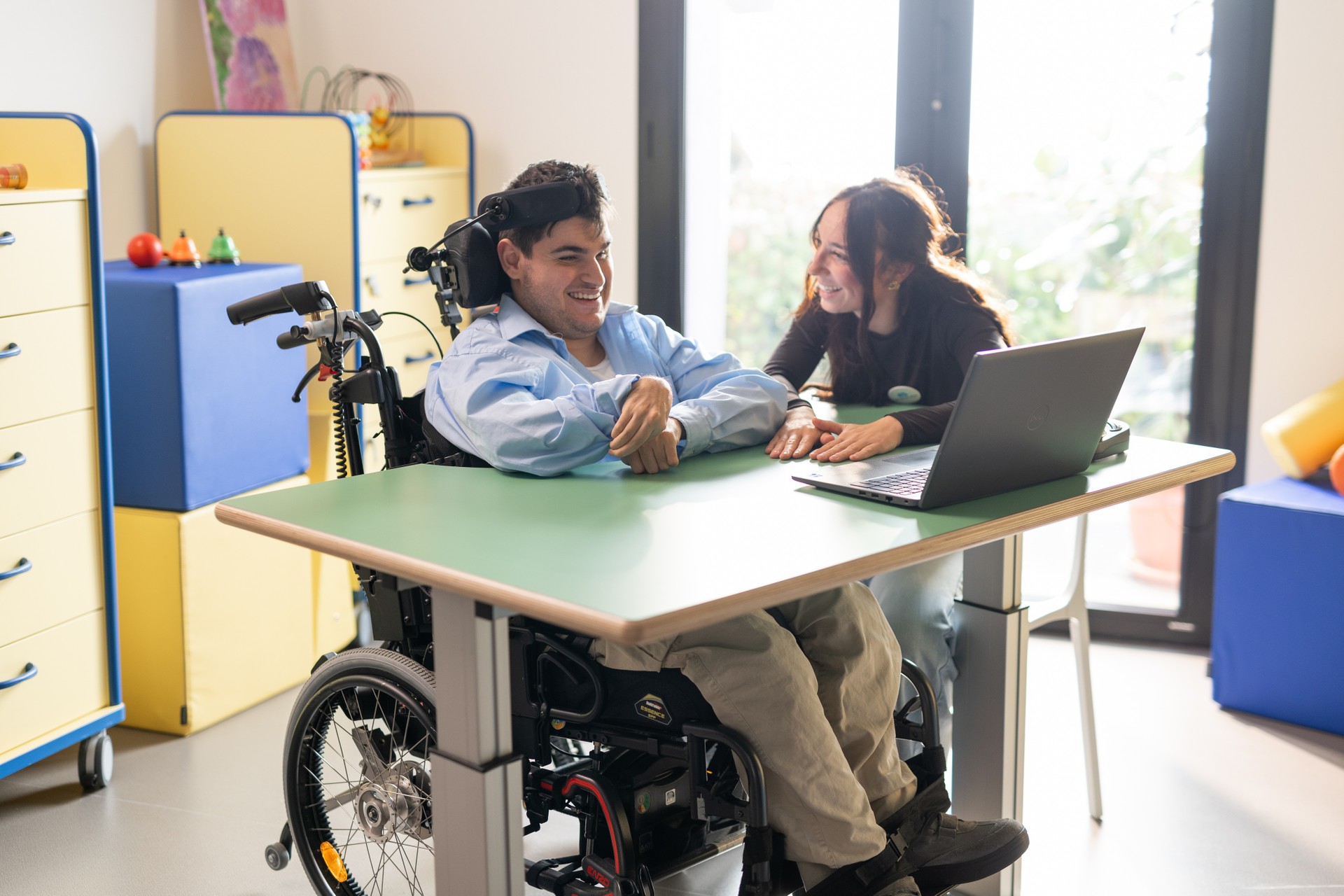 antonio è seduto dietro al tavolo sulla sua carrozzina, ed insieme alla sua educatrice sono davanti ad un pc portatile