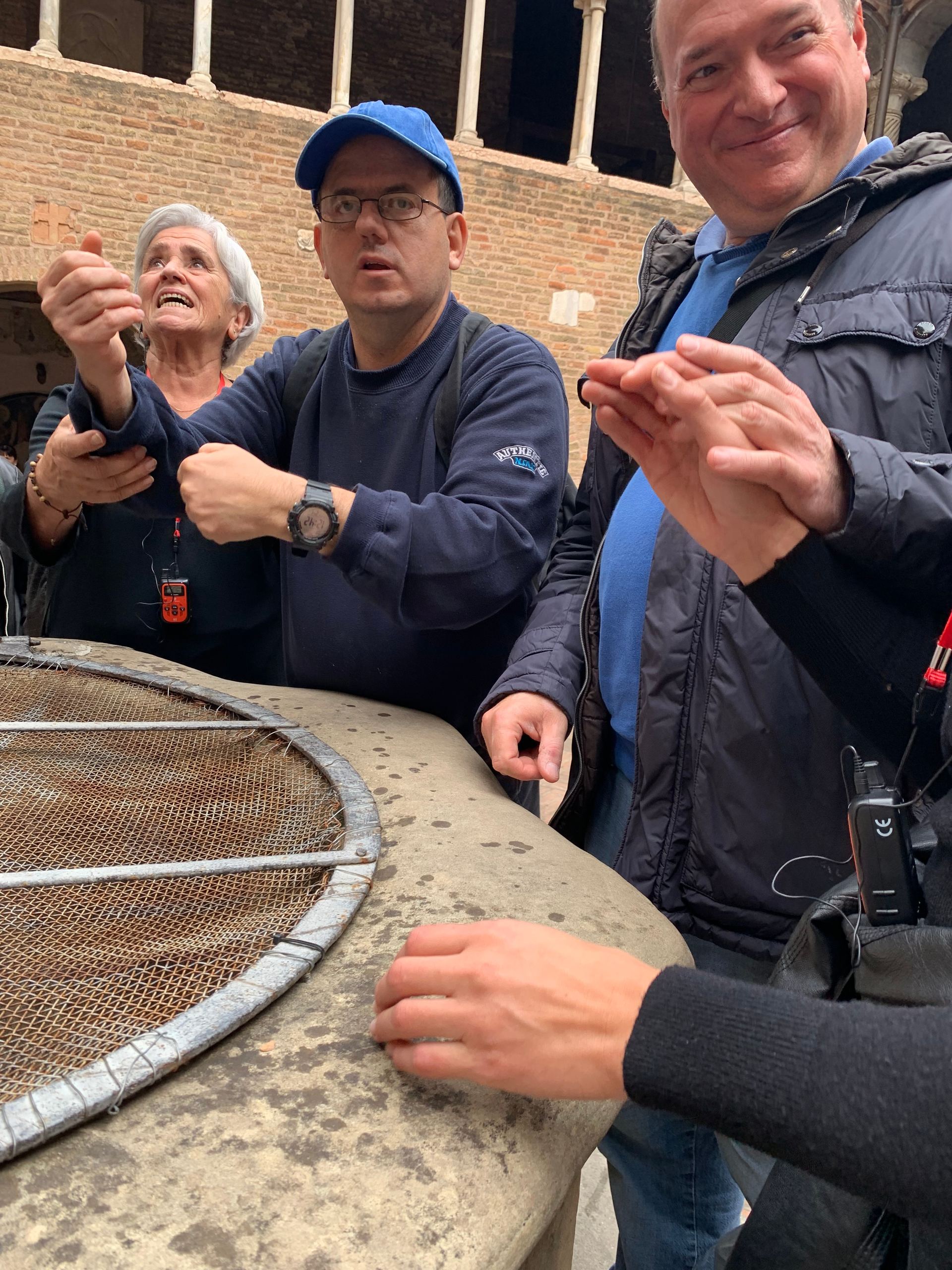 Un gruppo di utenti e volontari si raccoglie attorno al bordo di un pozzo protetto da una grata, situato al centro di un chiostro. 