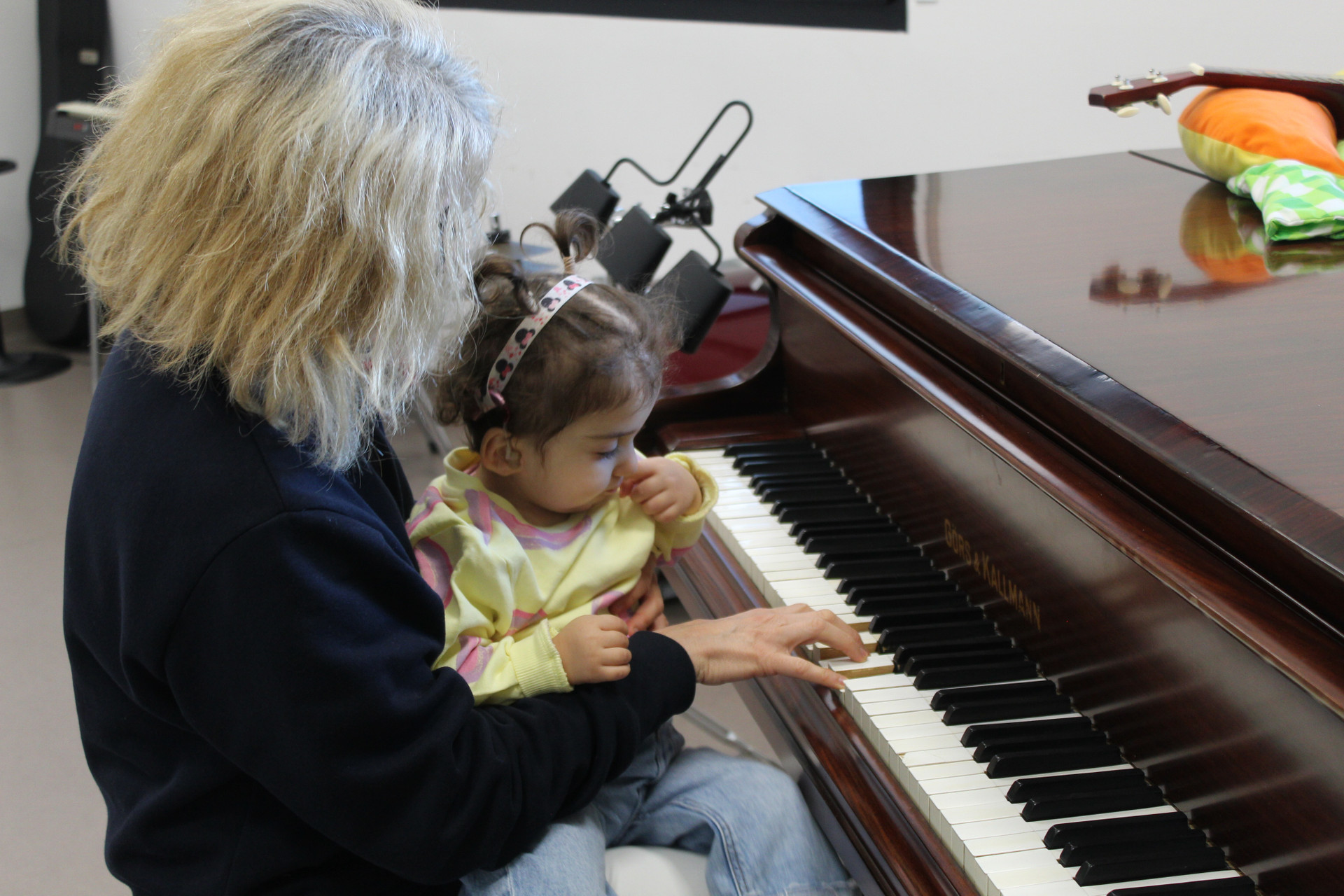 Sophie, bambina sordocieca con la sindrome di Charge, insieme alla musicoterapista Fiammetta. Fiammetta sta seduta al pianoforte con in braccio Sophie e preme sui tasti dello strumento 