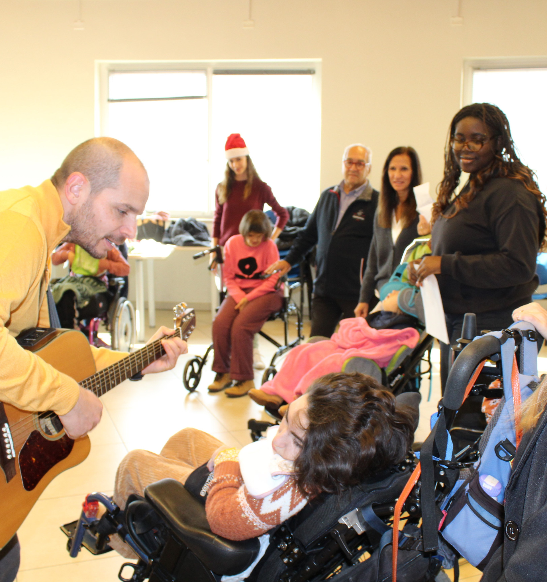 Un gruppo di utenti ed educatori festeggiano il Natale insieme cantando. Un educatore suona la chitarra e canta