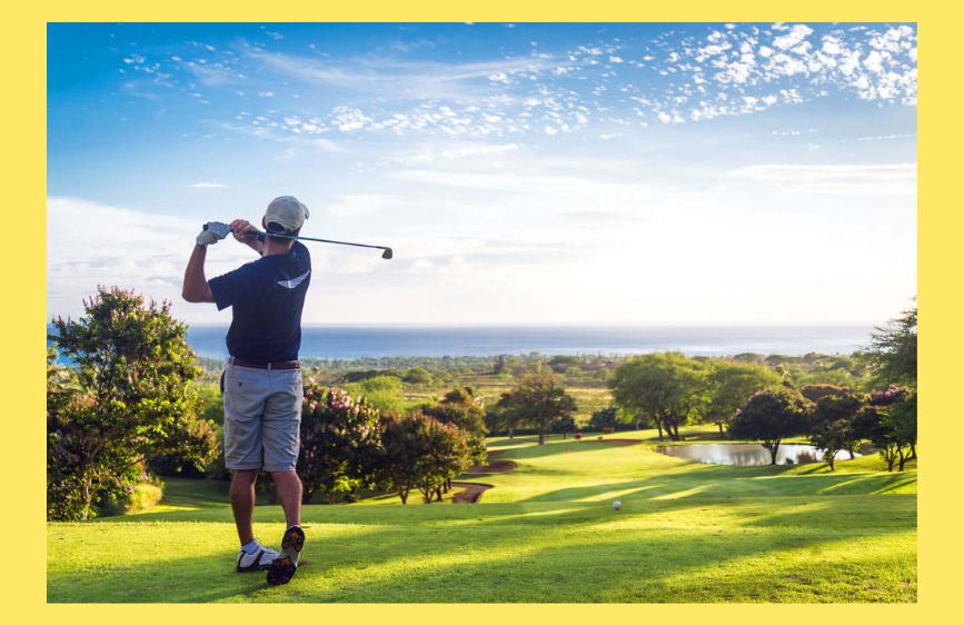 Golfista visto di spalle mentre colpisce la pallina su un campo verde con vista panoramica sul mare e cielo sereno punteggiato di nuvole.