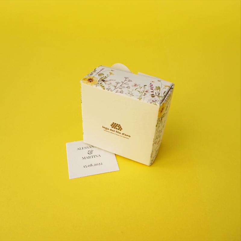 Bomboniera Floreale Lega del Filo d'Oro, in cartoncino bianco con una fantasia a fiori di campo e una romantica chiusura a cuore. Accompagnata da bigliettino personalizzabile
