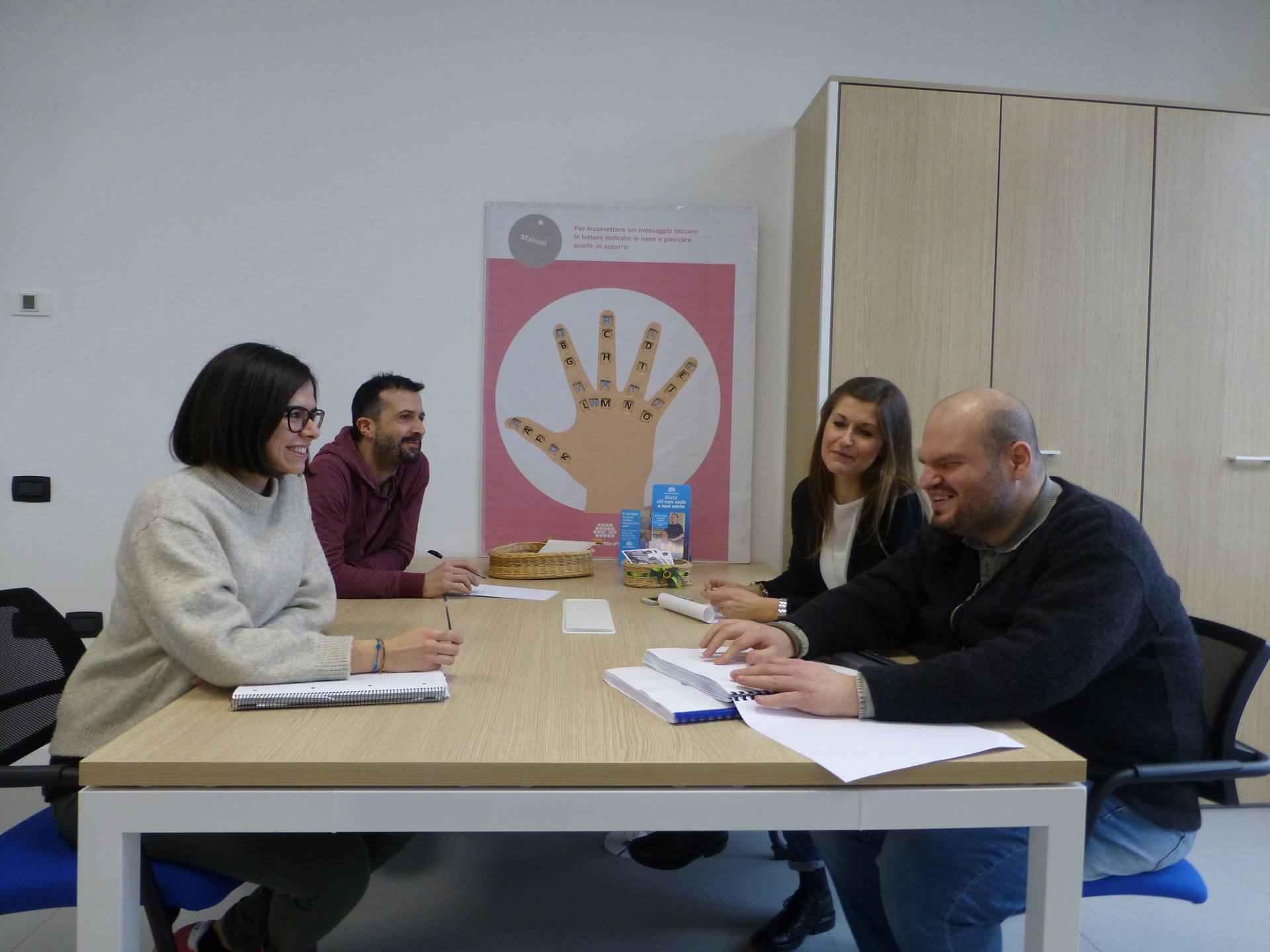 Quattro dipendenti seduti a un tavolo nell'ufficio Attività Associative e Volontariato del primo lotto, nel Centro Nazionale di Osimo