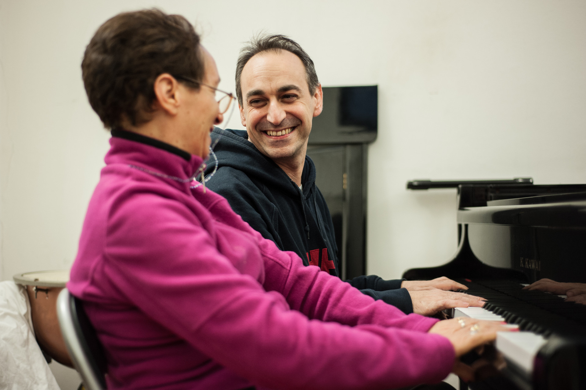 Un musicoterapista sorride guardando un’utente, ritratta di profilo, mentre suonano insieme il pianoforte.