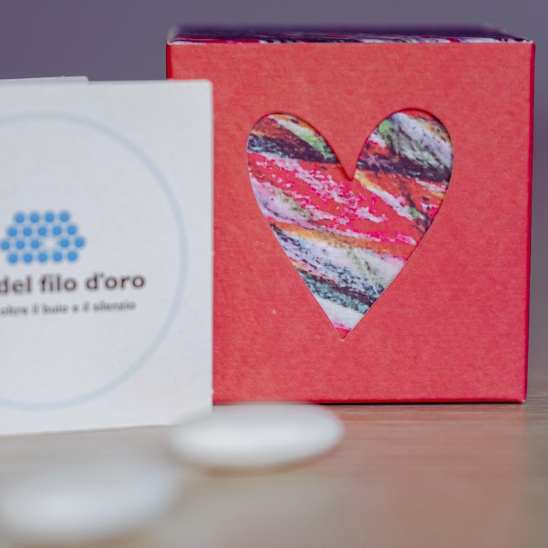 Bomboniera Cubo Pop composta da due scatoline in cartoncino pregiato inserite l'una nell'altra. Quella esterna è Rossa, quella interna, visibile da un'apertura a forma di cuore, ha una fantasia multicolore ispirata ai disegni degli ospiti della Lega del Filo d'Oro