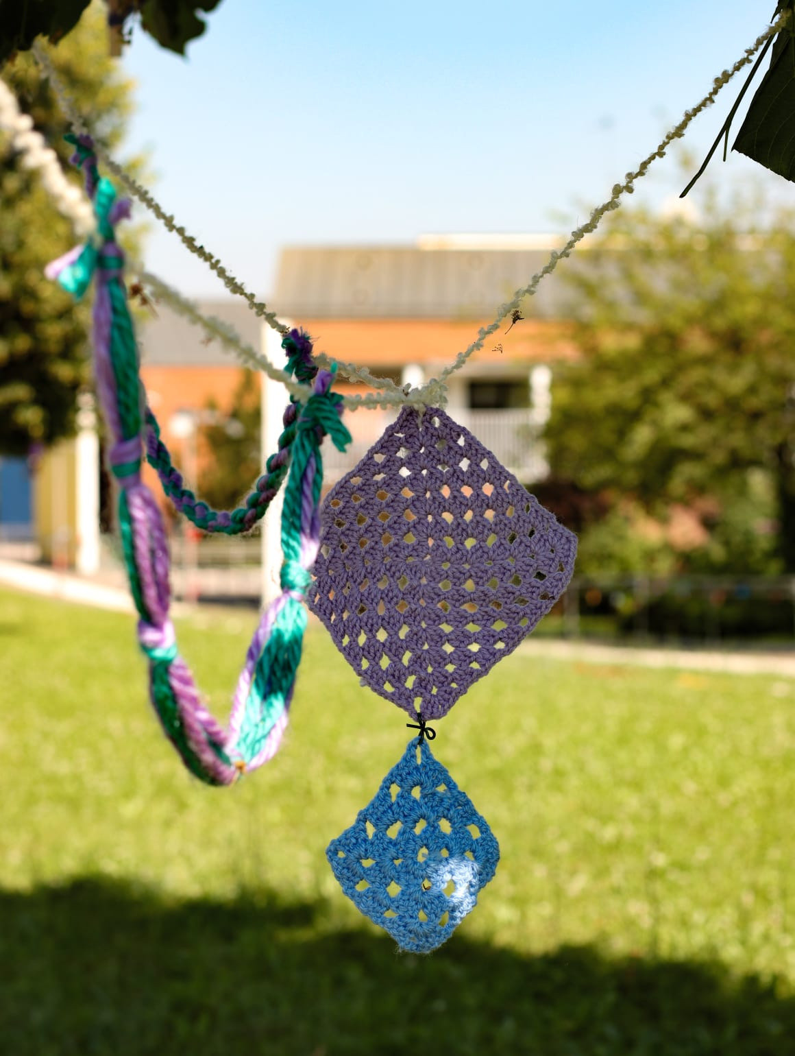 La Lega del Filo d’Oro ha aderito e promosso lo Yarn Bombing. Due creazioni a maglia a forma di rombo, una viola e una più piccola azzurra, sono appese a un filo. Accanto, una collana artigianale completa la composizione