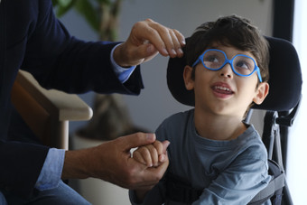 Il piccolo Nicola, bambino seguito dalla Lega del FIlo d'Oro, sorride mentre Neri Marcorè, testimonial dell'associazione, lo tiene per mano e gli sta per fare una carezza. Primo piano del bambino.