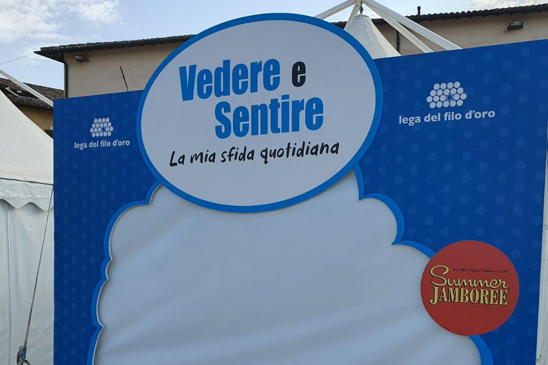 Lo stand della Lega del FIlo d'Oro al Summer Jamboree, blu con le scritte bianche. Sulla facciata c'è la scritta "Vedere e sentire la mia sfida quotidiana".