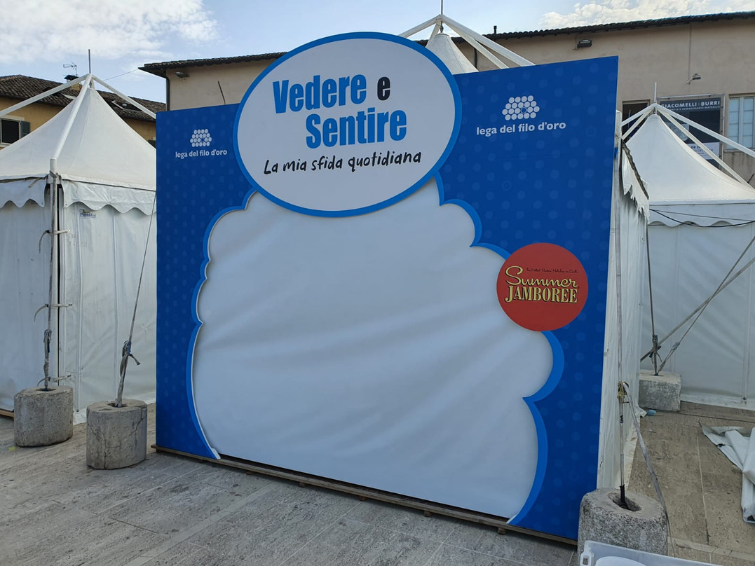 Lo stand della Lega del FIlo d'Oro al Summer Jamboree, blu con le scritte bianche. Sulla facciata c'è la scritta "Vedere e sentire la mia sfida quotidiana".