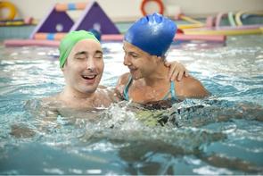 Un utente adulto della Lega del Filo d'Oro è ritratto mentre svolge un'attività in piscina insieme a un'operatrice. L'immagine cattura un momento di esercizio e supporto