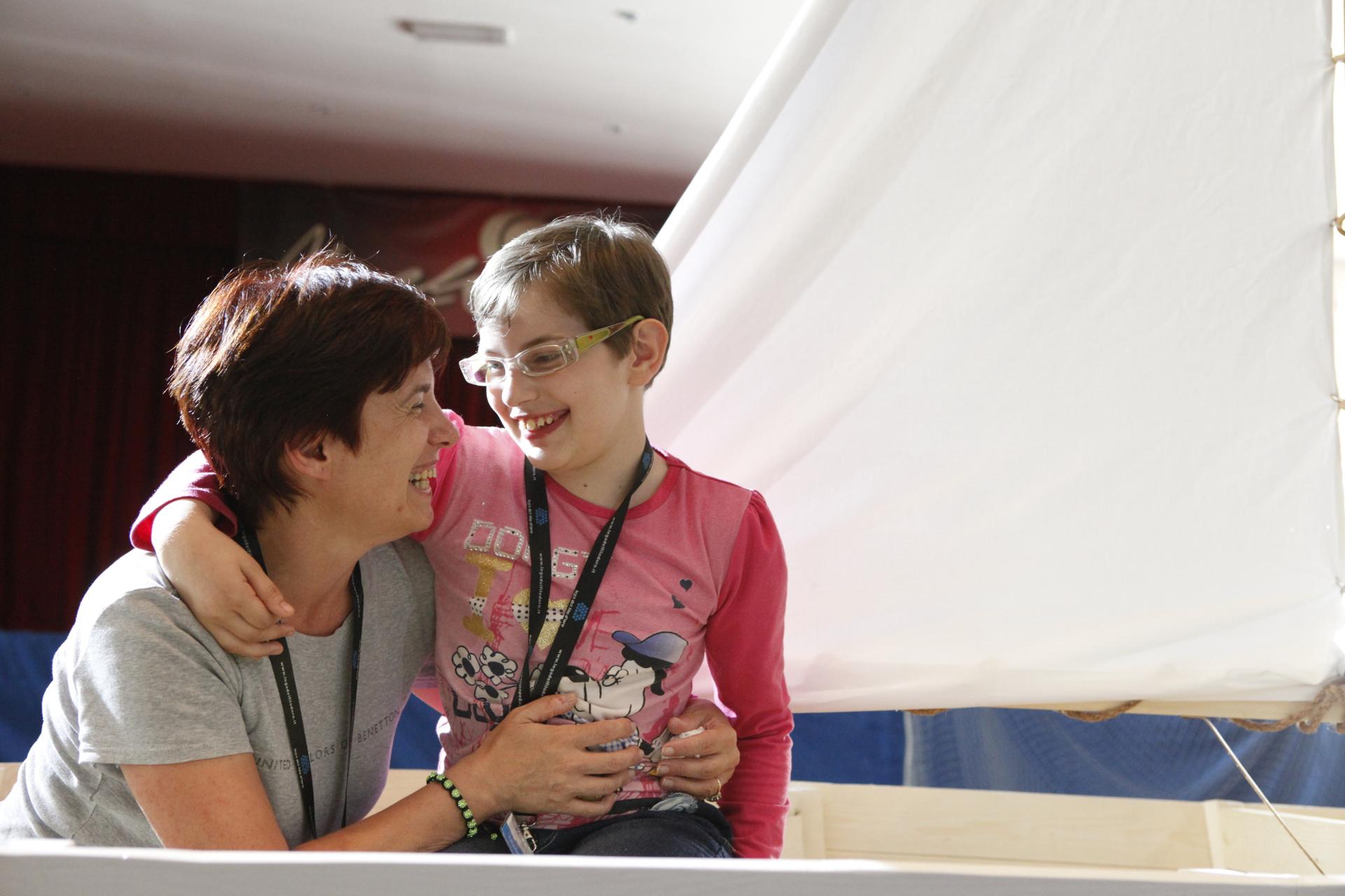 Una volontaria abbraccia una piccola utente, entrambe si guardano ridendo divertite