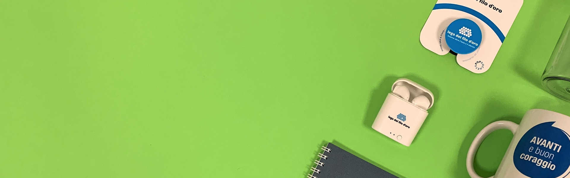 Composizione di regali solidali su sfondo verde, inclusi penna USB, auricolari wireless e bottiglietta in tritan. Perfetti per donare con stile e solidarietà.