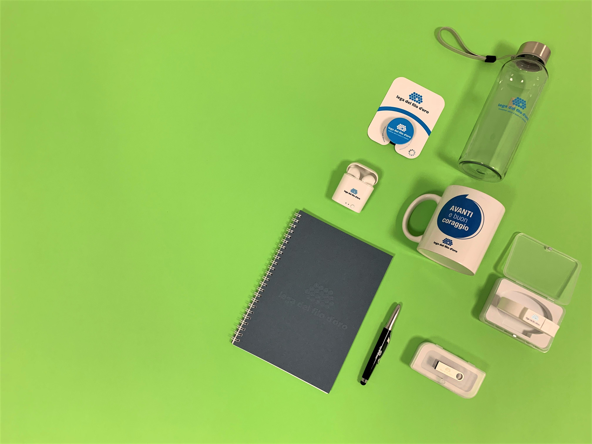 Composizione di regali solidali su sfondo verde, inclusi penna USB, auricolari wireless e bottiglietta in tritan. Perfetti per donare con stile e solidarietà.