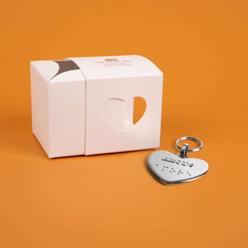 Bomboniera composta da due scatoline in cartoncino pregiato inserite l'una nell'altra. Quella esterna è bianca, quella interna, visibile da un'apertura a forma di cuore, è bianca. Accompagnata dal suo portachiavi cuore