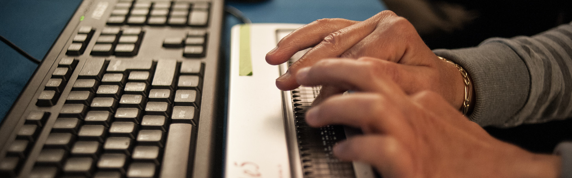Dettaglio di mani che leggono il testo di un pc grazie a una barra braille
