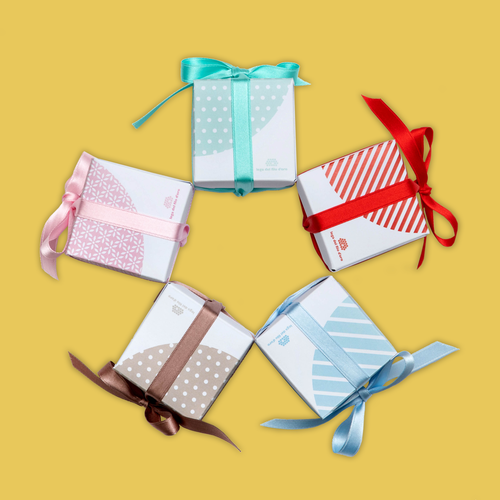 Bomboniere Pastello: foto di gruppo. Bomboniere cubiche in cartoncino bianco decorate con stampe di colori e fantasie diverse (rossa, azzurra, rosa, tortora, acquamarina) e fiocchetto in raso in tinta