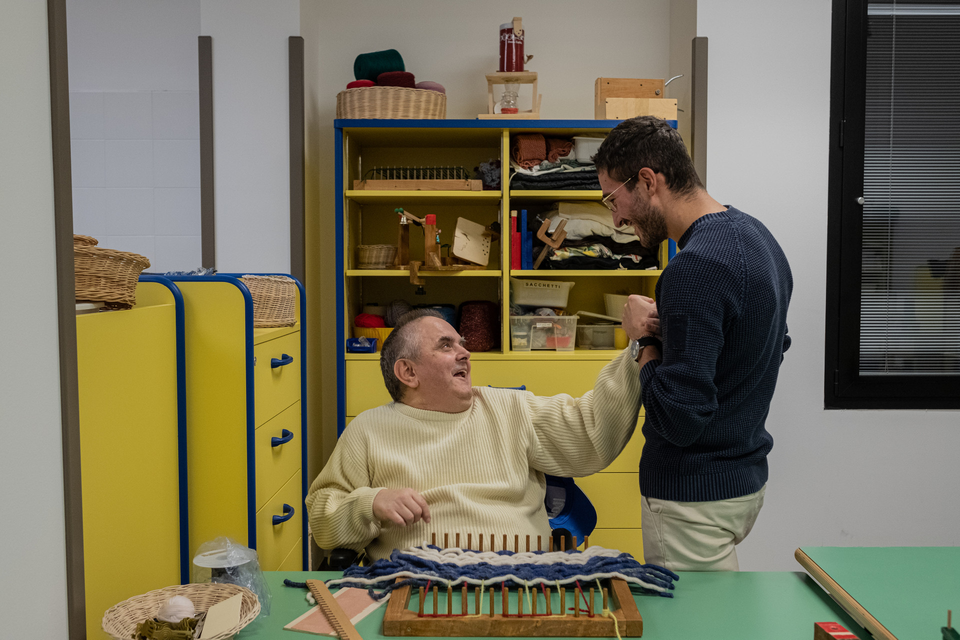 Fabio, ospite adulto del centro di Osimo, è seduto e sorride ad un operatore.