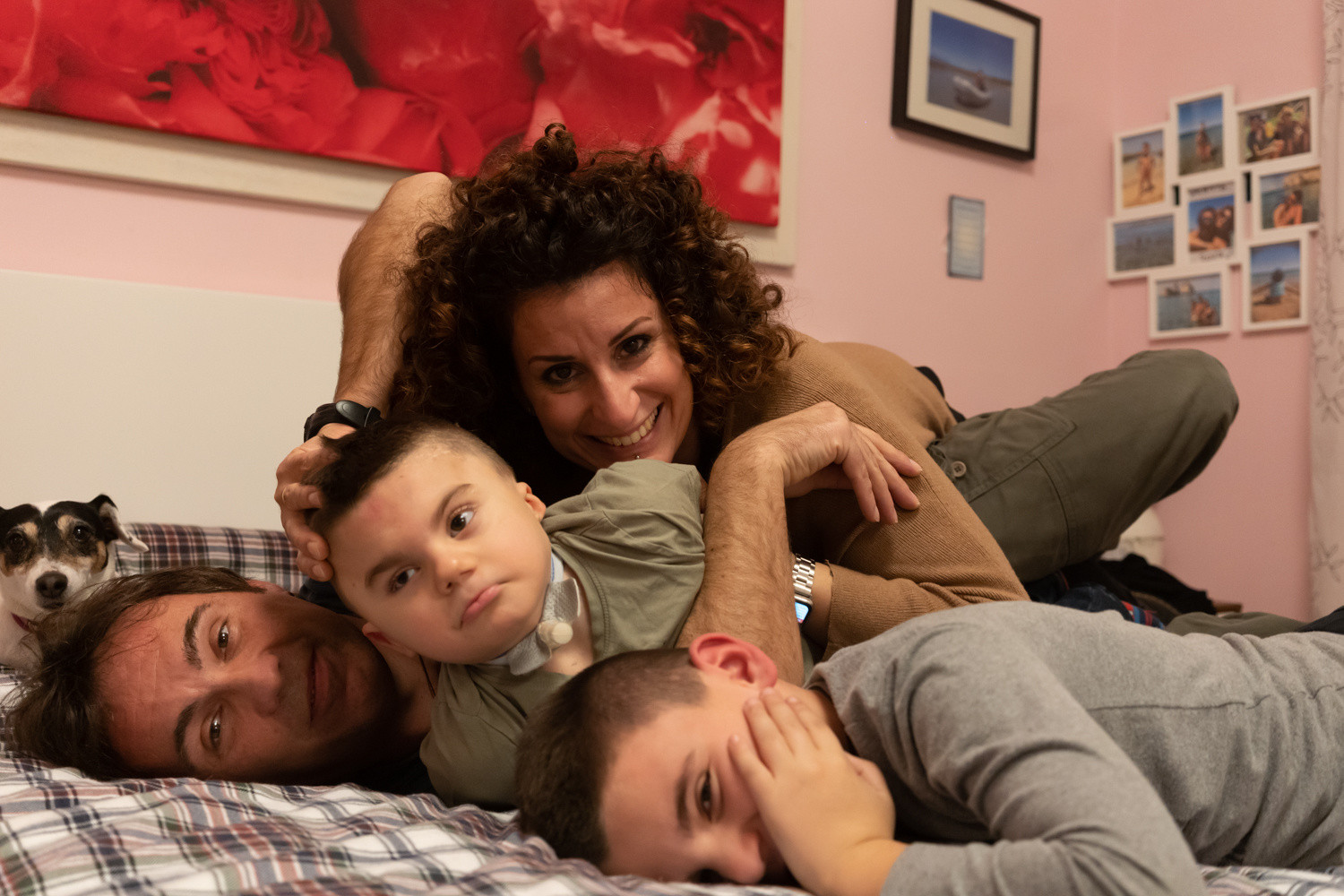 Foto della famiglia di Leonardo, un bambino affetto dalla sindrome di Charge, seguito dalla Lega del Filo d'Oro. Ci sono la mamma, il papà, Leonardo e il fratello maggiore e la loro piccola cagnolina. Sono stesi sul letto, sorridono alla camera