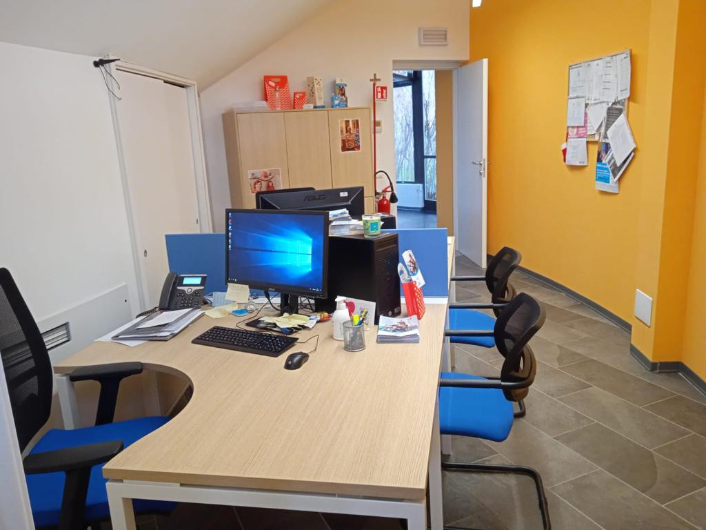 Sede di Novara: interno di un ufficio con tavoli, sedie e computer e muro arancione