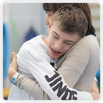 In questa foto, Filippo, ragazzo utente seguito dalla Lega del Filo d'Oro, abbraccia forte la sua educatrice e sorride.