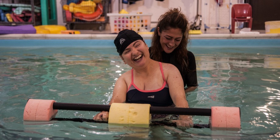 Paola, ospite residenziale al Centro Nazionale di Osimo, in piscina mentre fa idroterapia con la terapista, ridono divertite.